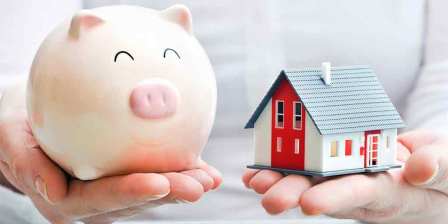 person holds piggy bank and model house