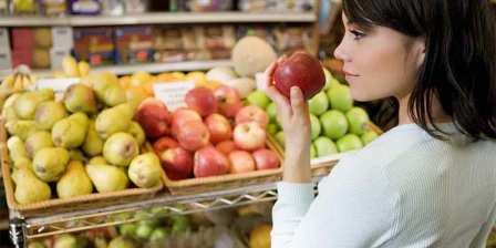 woman in supermarket picks up apple