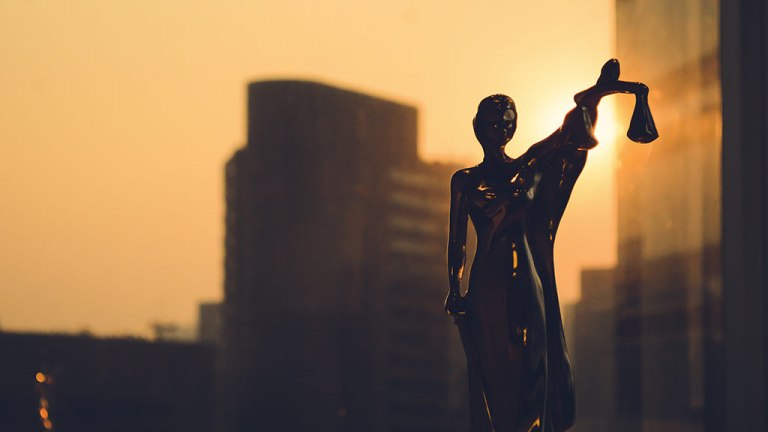 silhouette of themis statue with buildings in background