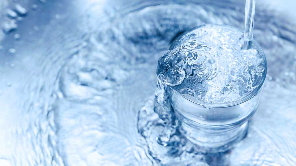 Water pouring into a glass and overflowing
