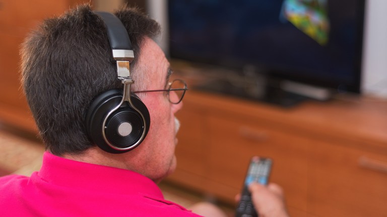 man_with_hearing_aid_and_headphones_watching_tv