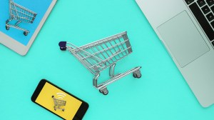 a laptop, tablet and smartphone with miniature shopping trolleys next to them