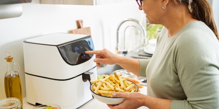 person putting large bowl of chips into air fryer