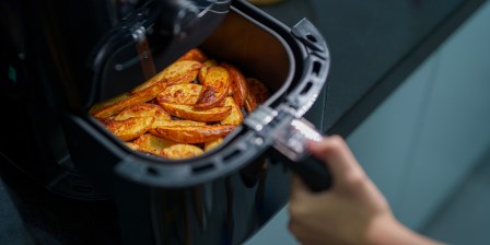 person removing air fryer basket with potato wedges to give it a shake