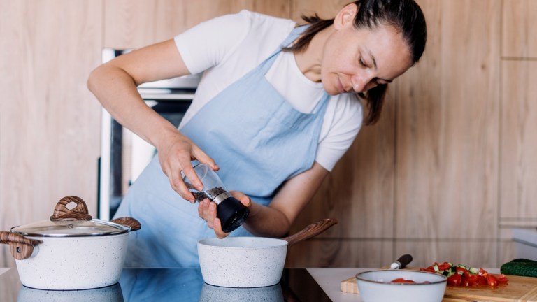 person adding pepper to a saucepan on an induction cooktop