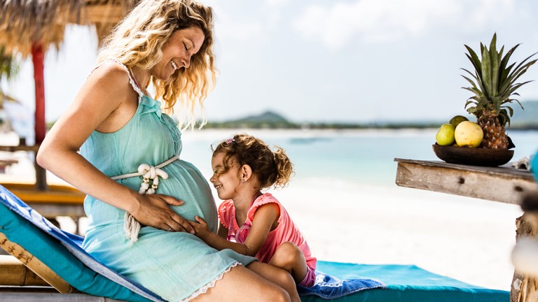 pregnant mother and daughter siting on deckchair at tropical beach