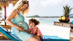 pregnant mother and daughter siting on deckchair at tropical beach